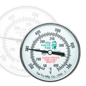 Ein rundes analoges Grillthermometer der Marke Big Green Egg mit Temperaturanzeige in Fahrenheit und Celsius. In der Mitte befindet sich ein Warnhinweis in roter Schrift. Im Hintergrund ist das gleiche Thermometer transparent gespiegelt.