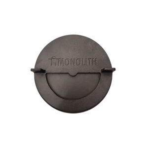 Runder, schwarzer Metalldeckel mit der Aufschrift MONOLITH und einem stilisierten Grill-Symbol. Der Deckel besitzt zwei seitliche Griffe und eine halbkreisförmige Öffnung in der Mitte, die verschliessbar wirkt. Oberfläche leicht strukturiert.